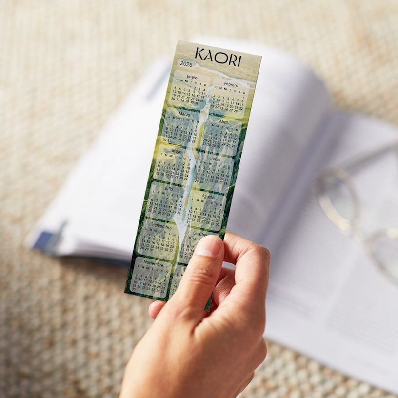 Una persona sujetando un calendario marcapáginas del 2026 con un diseño verde, colocado sobre un libro abierto.