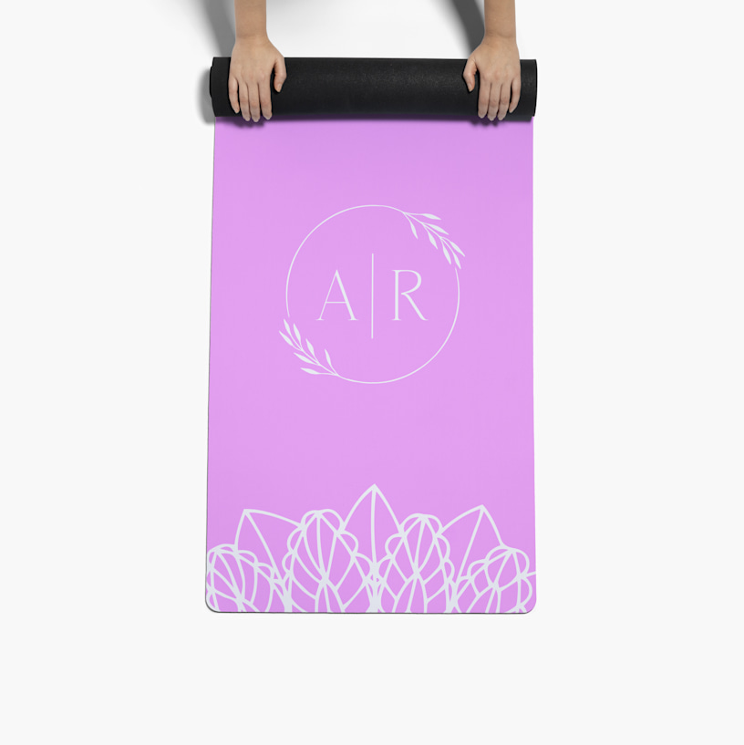 Un par de manos desenrollando una esterilla de yoga personalizada impresa con un monograma. 