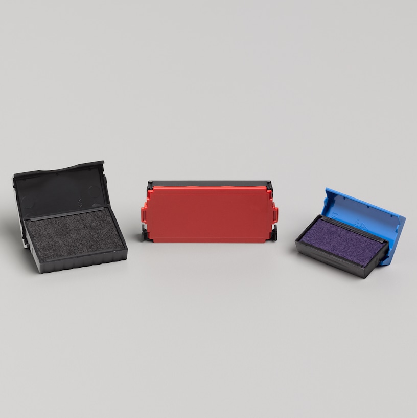 Una almohadilla rectangular de repuesto de tinta negra mediana, una roja grande y una azul pequeña en sus estuches plegables.