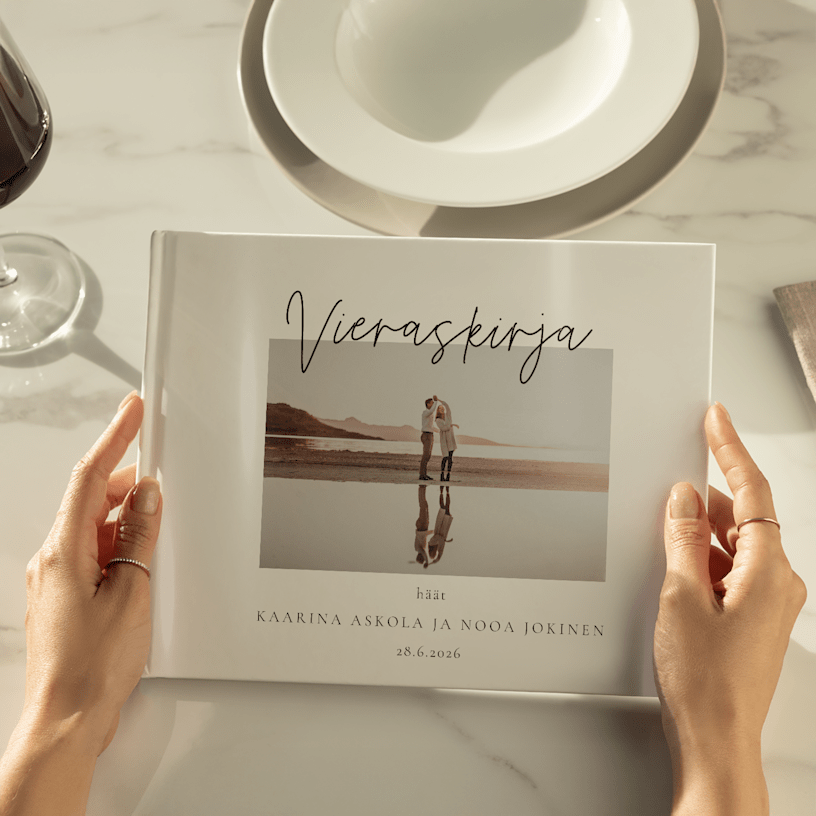 Kädet pitelevät häävieraskirjaa, jonka kannessa on kuva pariskunnasta. 