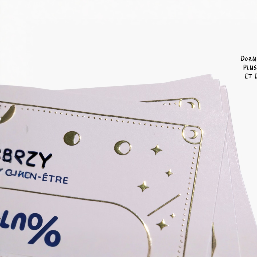 Gros plan sur une carte de visite présentant un logo et du texte mis en valeur par un effet métallisé doré en relief.