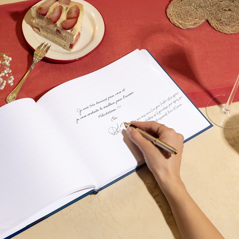 Une main en train de signer un livre d’or ouvert. 