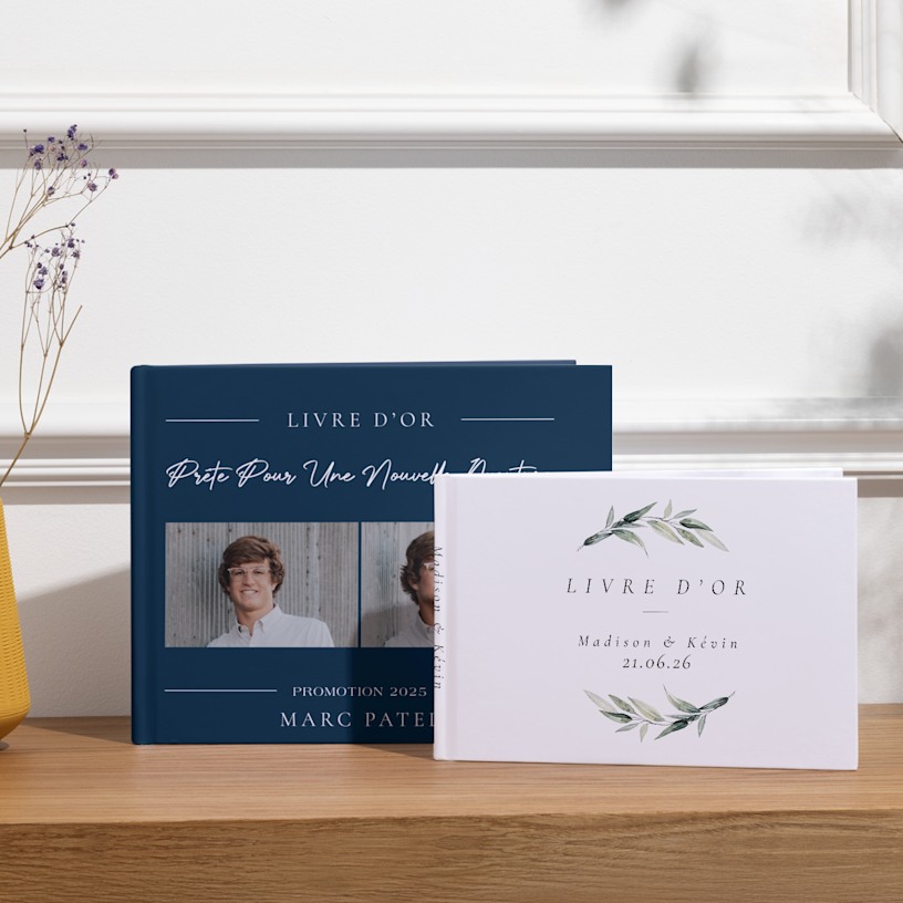 Deux livres d’or présentés sur une table, le premier est personnalisé pour une remise de diplôme et l’autre pour un mariage. 