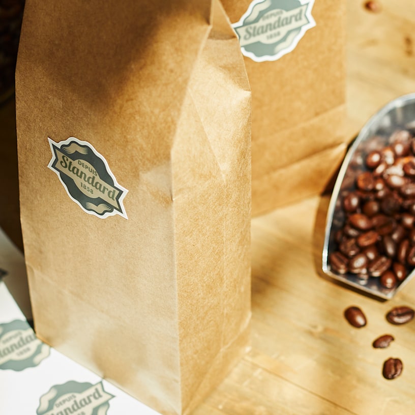 Deux sacs de grains de café accompagnés d’une feuille d’autocollants en forme de ruban, avec des autocollants provenant de la feuille collés sur le côté de chaque sac.
