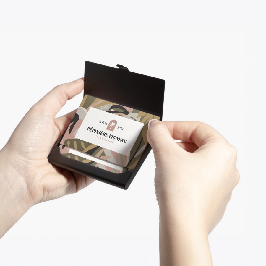 Une personne tenant un porte-cartes d’affaires en aluminium noir laissant apparaître les cartes d’affaires d’une entreprise de jardinage.