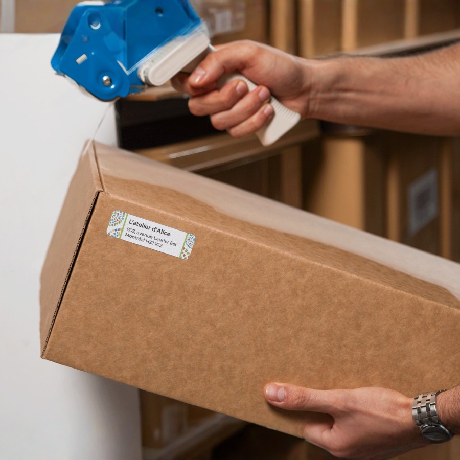 Une personne en train d’utiliser une étiqueteuse pour apposer des étiquettes d’adresse de retour sur un colis.