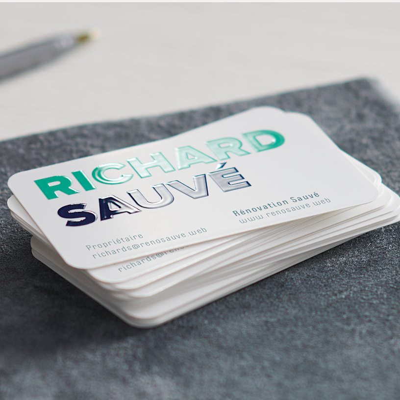 Une pile de cartes d’affaires rectangulaires aux coins arrondis, créées pour une entreprise de rénovation résidentielle, avec le nom Richard Suarez inscrit en relief en lettres brillantes et imposantes.