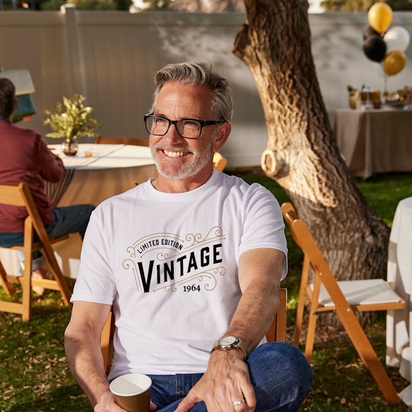 Un homme assis lors d’une célébration en plein air et portant un t-shirt d’anniversaire personnalisé. 