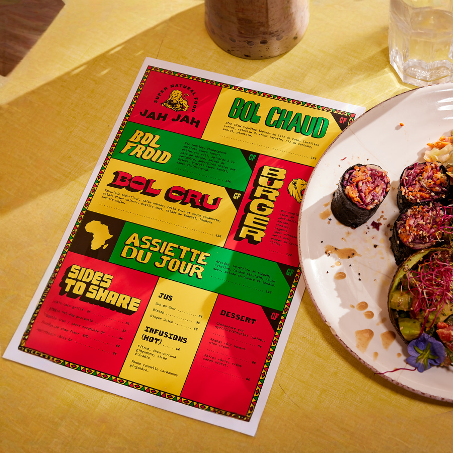 Menu coloré d’une page, posé sur une table de restaurant à côté d’un plat. 