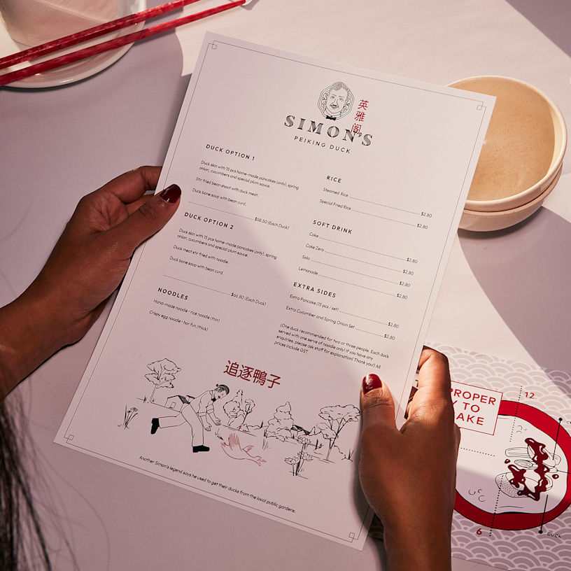 Client tenant le menu d’un restaurant chinois, juste au-dessus de son couvert.