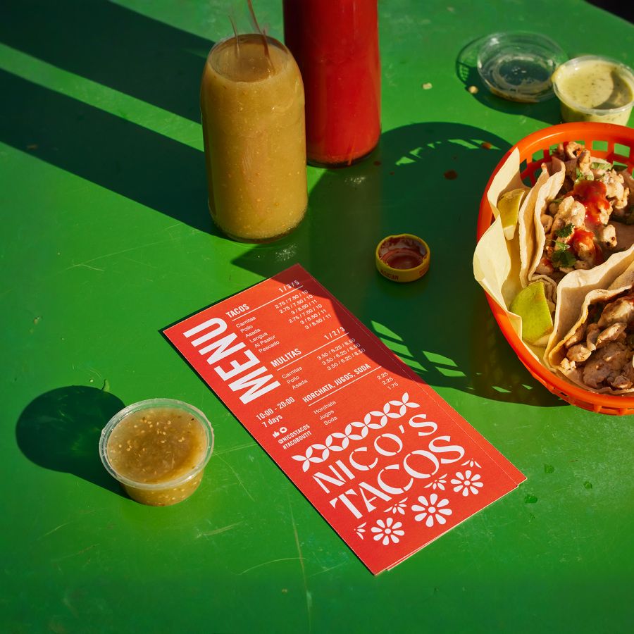 Menu d’une page pour un restaurant de tacos, posé sur une table à côté de bols de sauce et d’un panier de tacos.