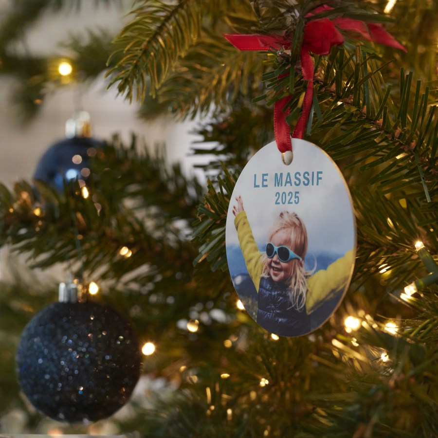 Une décoration originale sur un sapin de Noël avec la photo d’une petite fille portant des lunettes de soleil.  