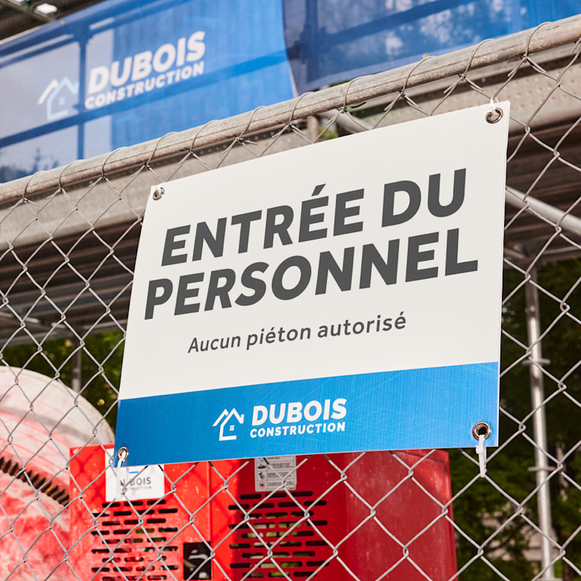 Une pancarte d’extérieur pour une entreprise de construction, suspendue à une clôture à l’aide d’œillets.