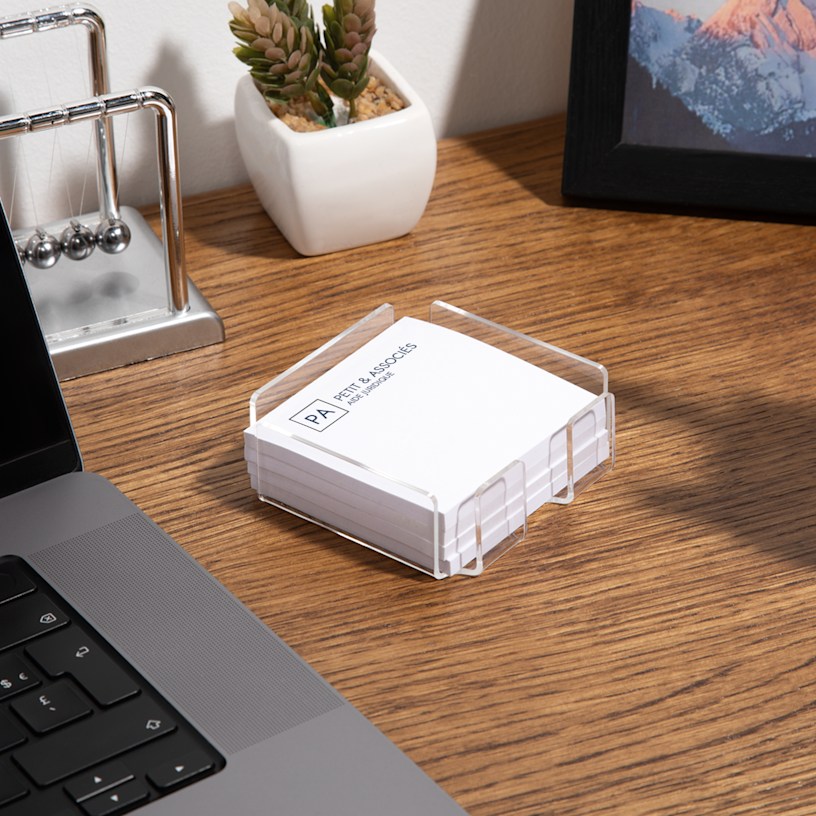 Un support en acrylique pour notes Post-ItMD posé sur un bureau à côté d’un ordinateur portable et rempli de papillons adhésifs Post-itMD personnalisés pour un cabinet d’avocats.