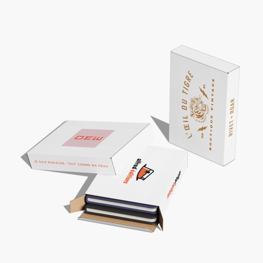 Trois boîtes d’expédition plates avec logo, dont une est remplie de cahiers.