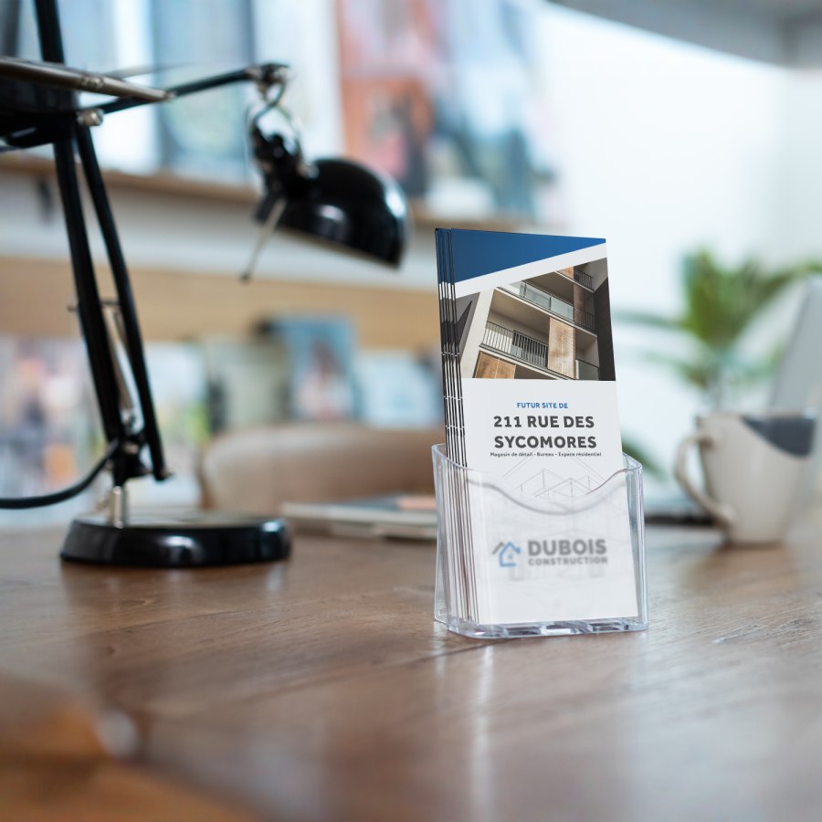 Une pile de dépliants à plis accordéon présentant une entreprise de construction, placée dans un porte-dépliants transparent, disposé dans un bureau.