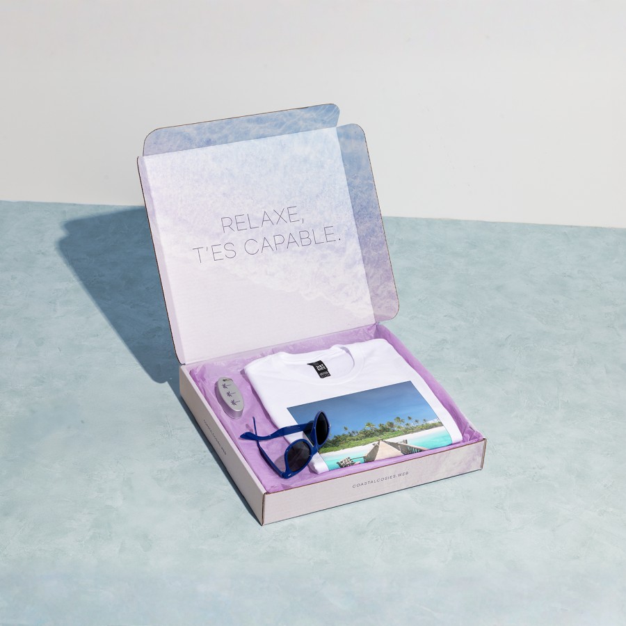 Une boîte carrée pour envoi postal remplie d’articles publicitaires pour une agence de voyages.