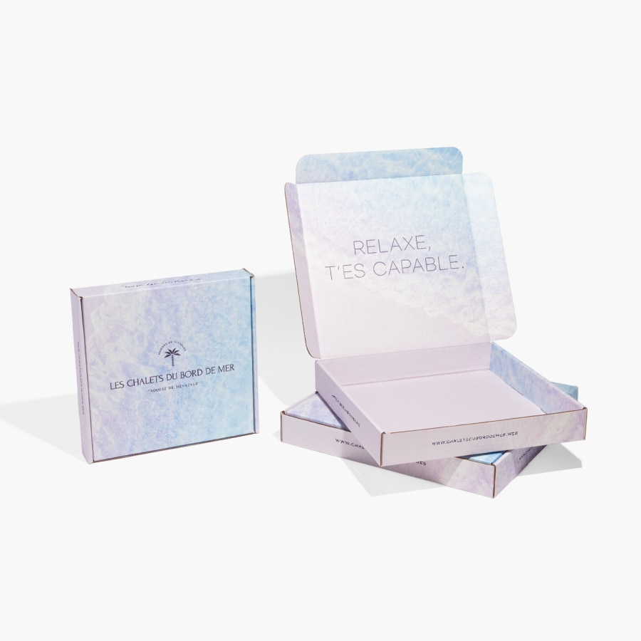 Trois boîtes carrées pour envoi postal, dont deux sont posées à plat et la troisième est dressée sur la tranche. La boîte du haut, posée à plat, est ouverte et dévoile un message à l’intérieur.