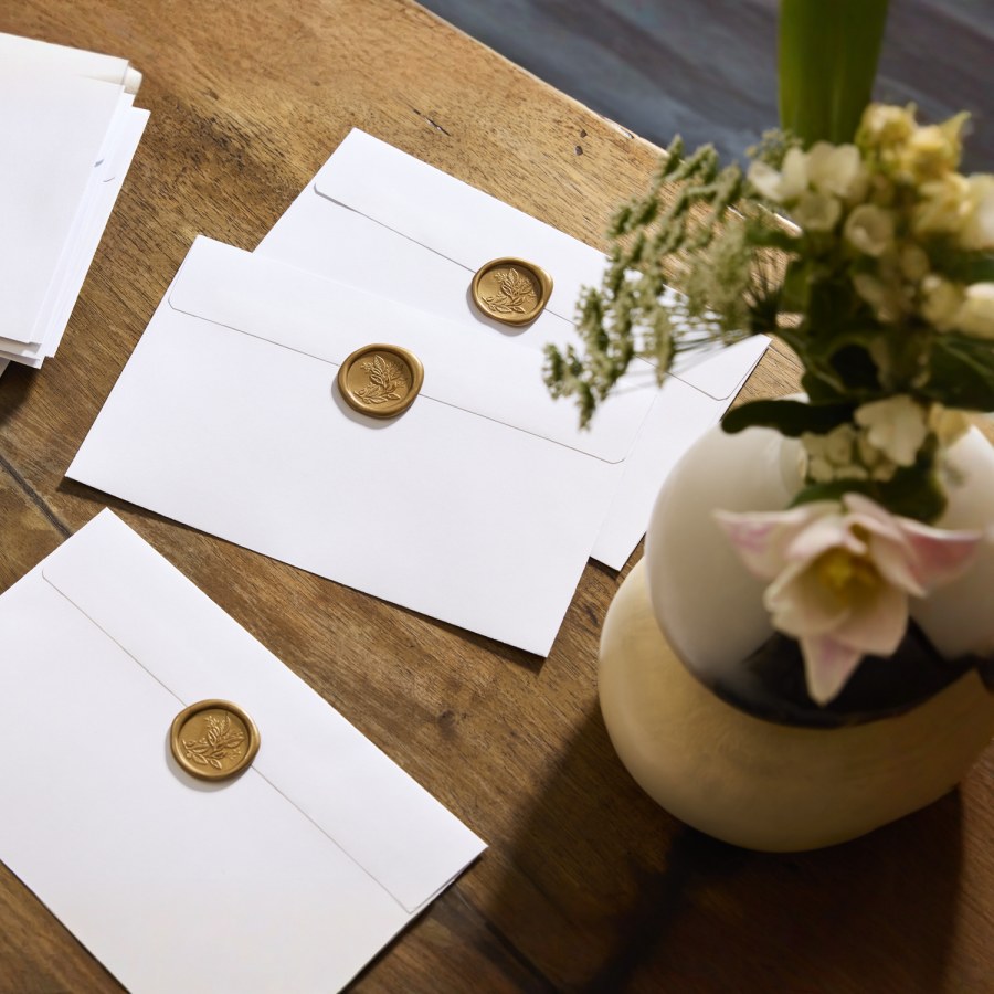 Des enveloppes blanches scellées avec des cachets de cire floraux de couleur or.