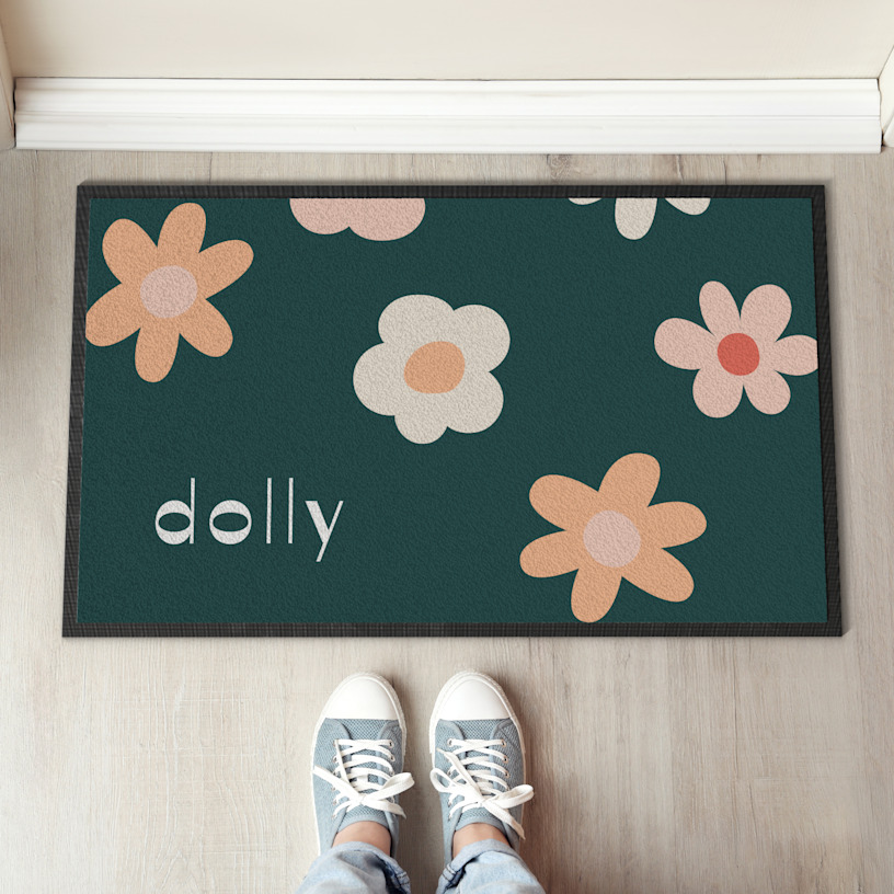 Une paire de chaussures de sport marron s’approche d’un tapis de sol à motif floral affichant le nom « Dolly ».