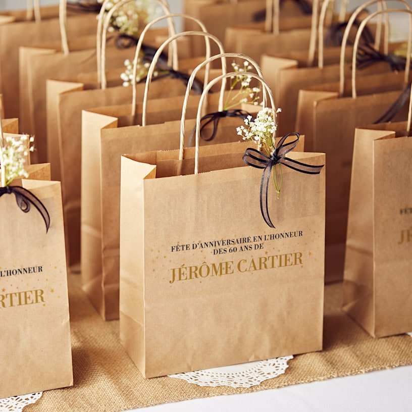 Une table de sacs de fête marrons à un anniversaire, décorés de fleurs et de rubans.