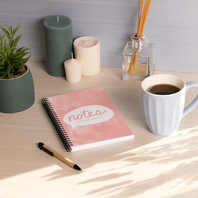 Un cahier personnalisé posé sur un bureau, entouré de café, de chandelles et d’autres objets.