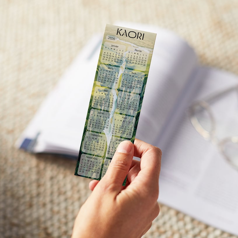 Une personne tenant un calendrier signet 2026 orné d’un design vert, posé sur un livre ouvert.