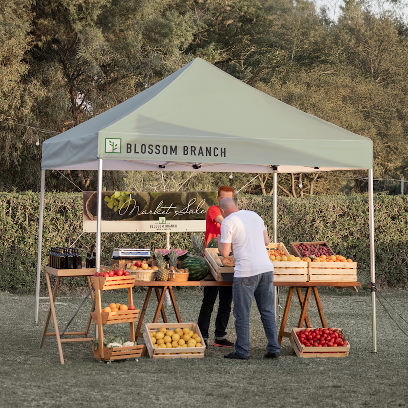 Un kiosque de fruits et légumes installé sous une tente publicitaire dans un marché en plein air.