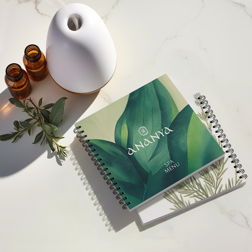 Catalogues de spa et bien-être avec reliure métallique, ornés de motifs botaniques et entourés d’un diffuseur et d’huiles essentielles.