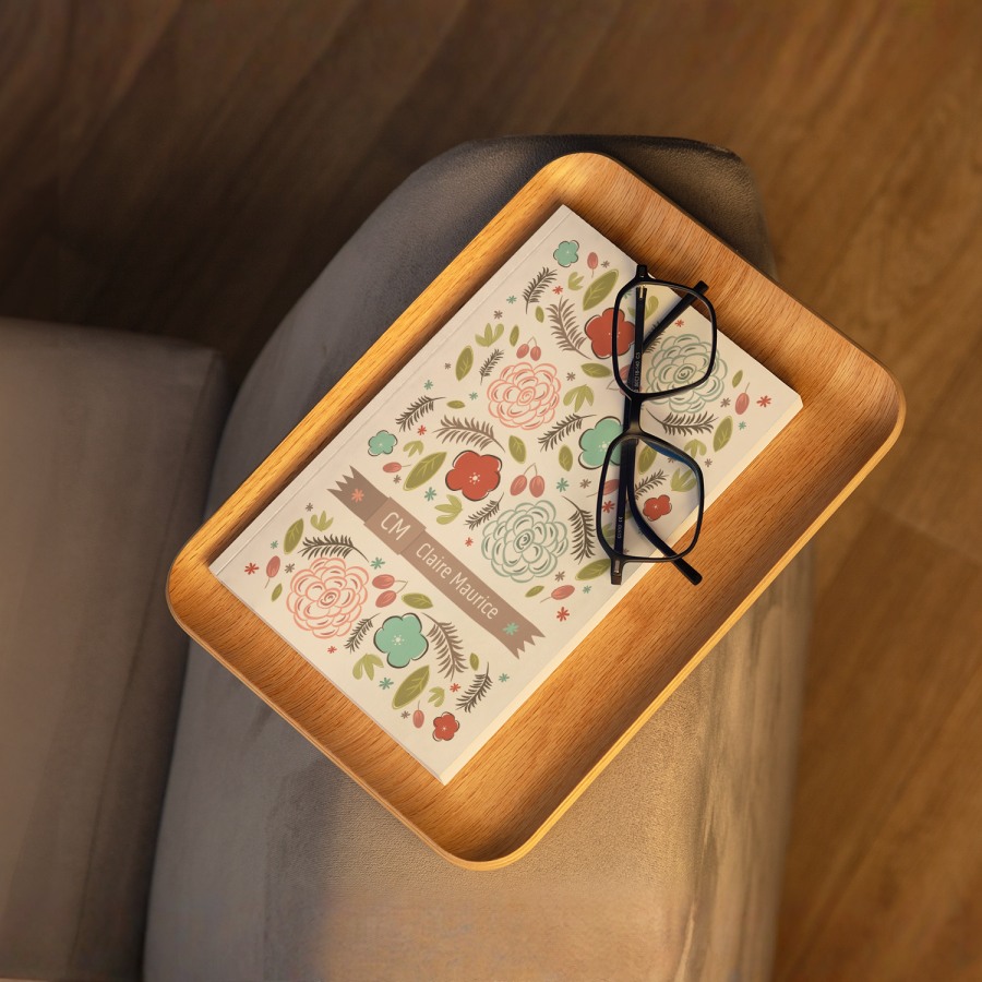 Un diario personalizado con una tapa con diseño de flores y un par de lentes de lectura, colocados sobre un sofá. 