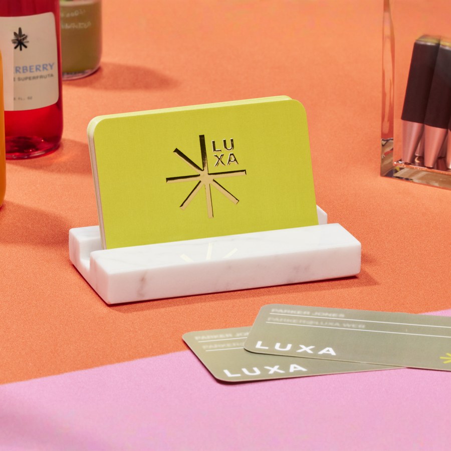 Cartes de visite effet métallisé en relief d’un restaurant ou d’une entreprise en lien avec l’alimentation, placées sur un porte-cartes de visite en marbre.