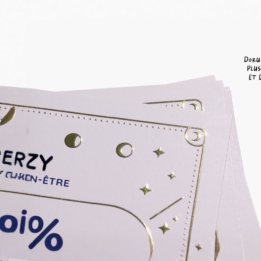 Gros plan sur une carte de visite présentant un logo et du texte mis en valeur par un effet métallisé doré en relief.