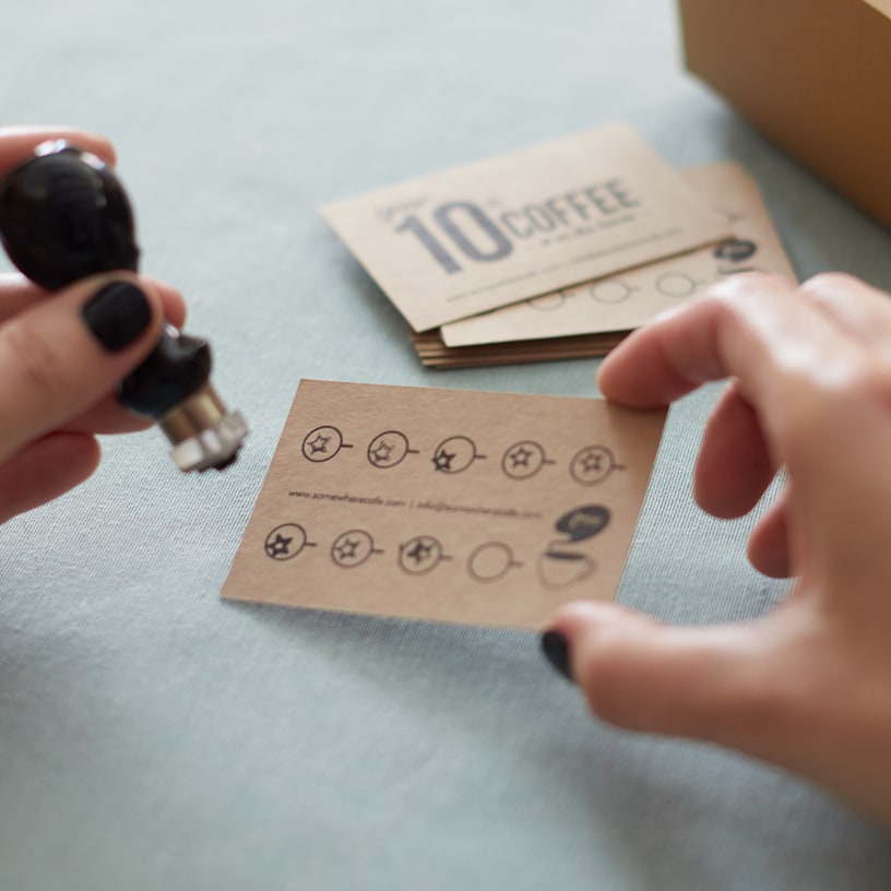 Une carte de visite en papier kraft pour un café faisant office de carte de fidélité, avec une main sur le point de tamponner la carte.