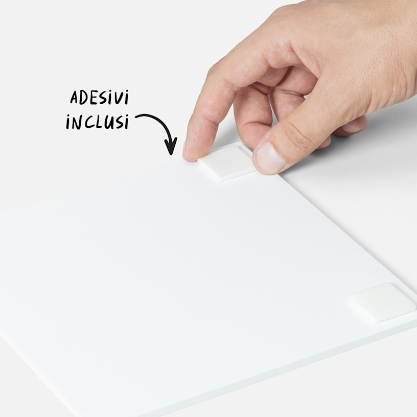 Una mano che applica nastro biadesivo sul retro di una foto su pannelli, accompagnata da un testo che indica che il nastro biadesivo è compreso. 