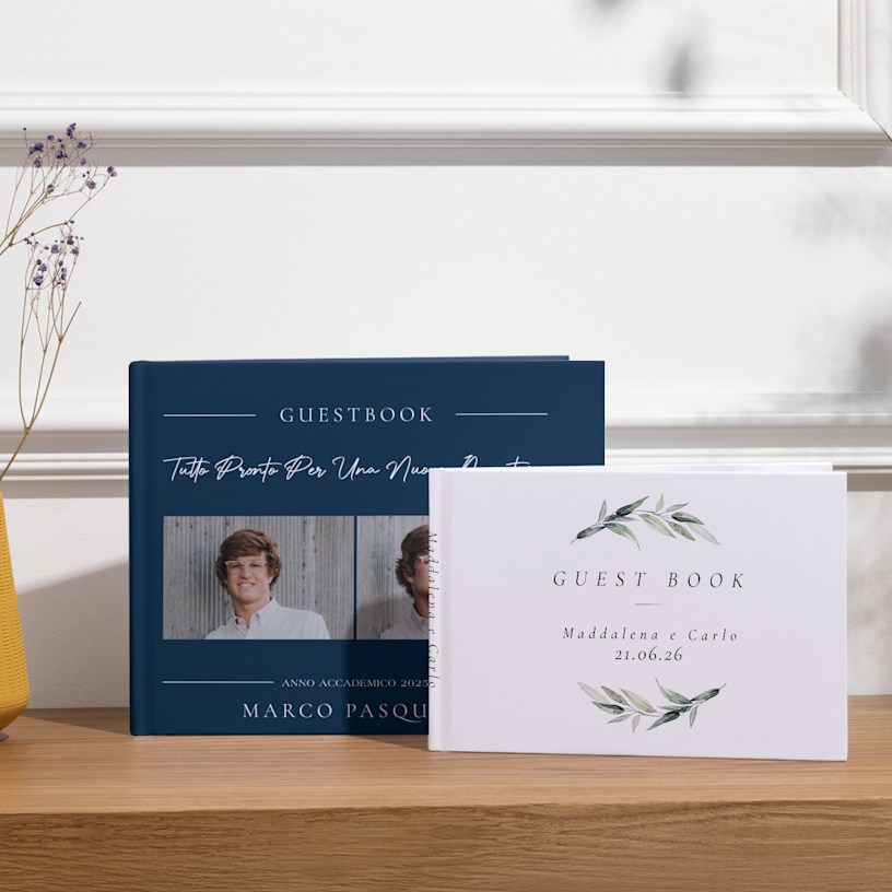 Due guestbook personalizzati esposti su un tavolo, di cui uno personalizzato per una festa di laurea e l’altro per un matrimonio. 