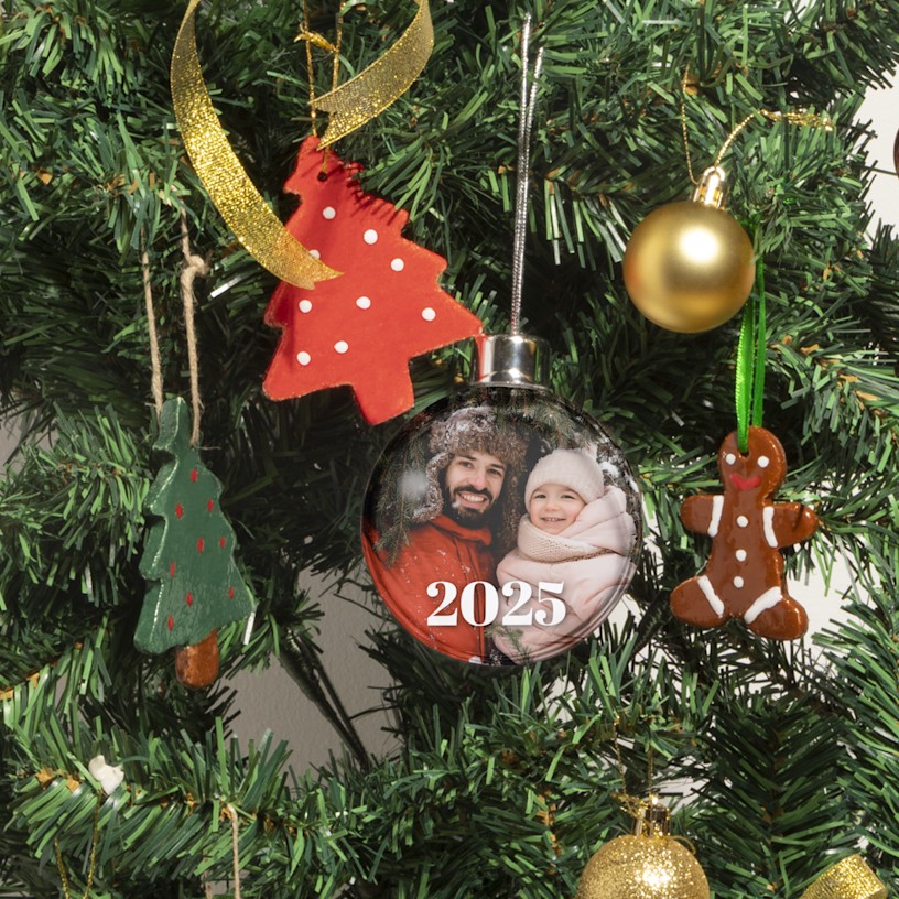 Una pallina di Natale appesa a un albero di Natale, personalizzata con la stampa di una foto che ritrae padre e figlia in abiti invernali. 