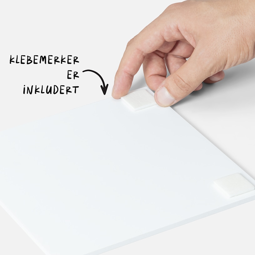 En hånd plasserer en dobbeltsidig teip på baksiden av en fotoflis, med en merknad om at teipen er inkludert med flisene. 