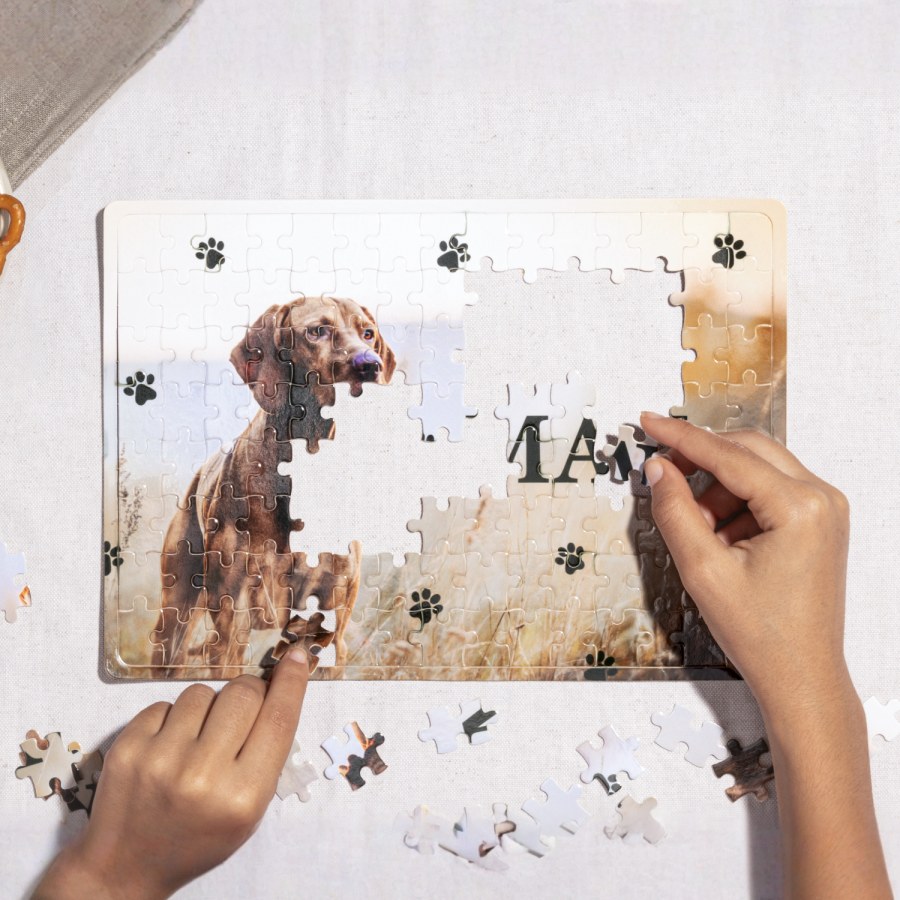 Een paar handen die een bedrukte puzzel van een hond maken op een tafelblad. 