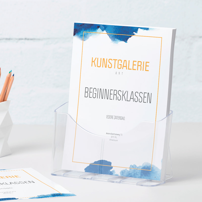 Een plastic A4-brochurehouder met flyers van een galerie staat naast een pennenbak op een bureau.