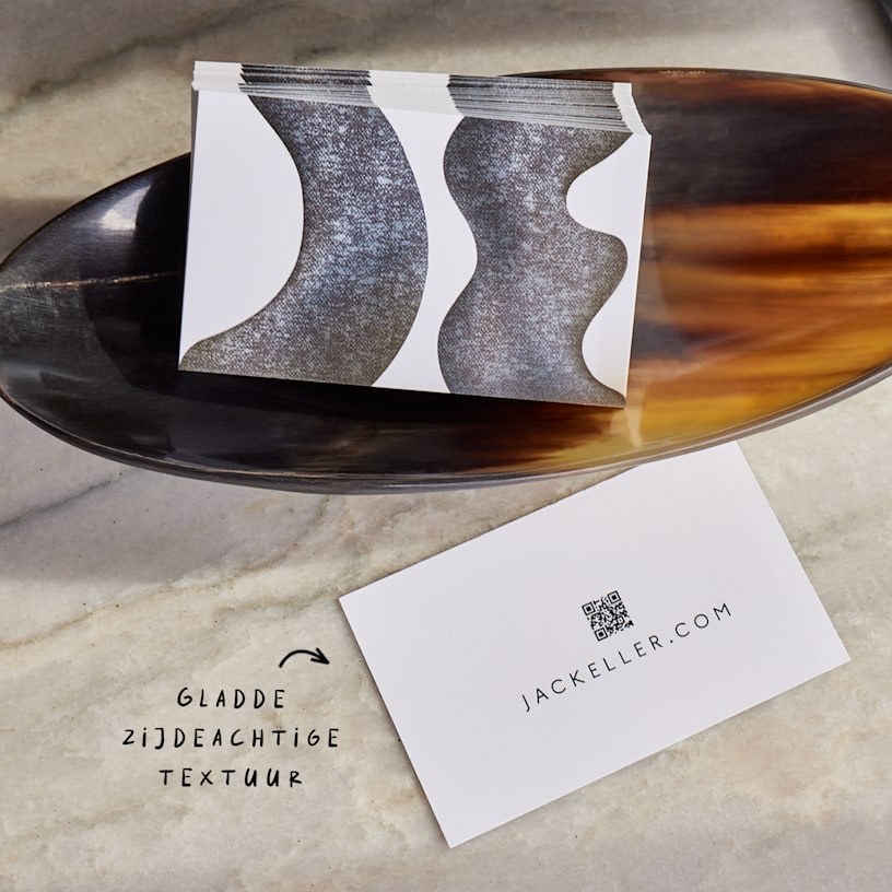Een stapel matte visitekaartjes in een houten schaal, met een notitie die op de zijdezachte textuur wijst.