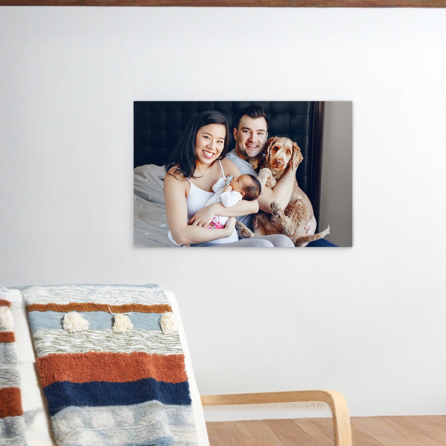 Uma impressão em acrílico que mostra uma fotografia de uma família, com dois pais, um bebé e um cão. 