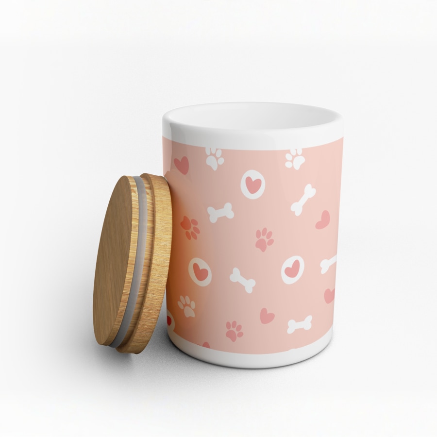 Um frasco para guloseimas cor-de-rosa e branco personalizado com desenhos de ossos para cães, impressões de patas e corações.