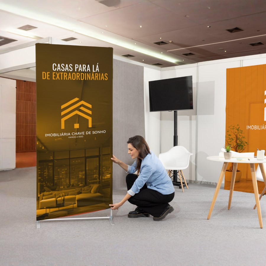 Uma pessoa numa exposição a montar um suporte em tubo para lona publicitária que promove um negócio imobiliário.