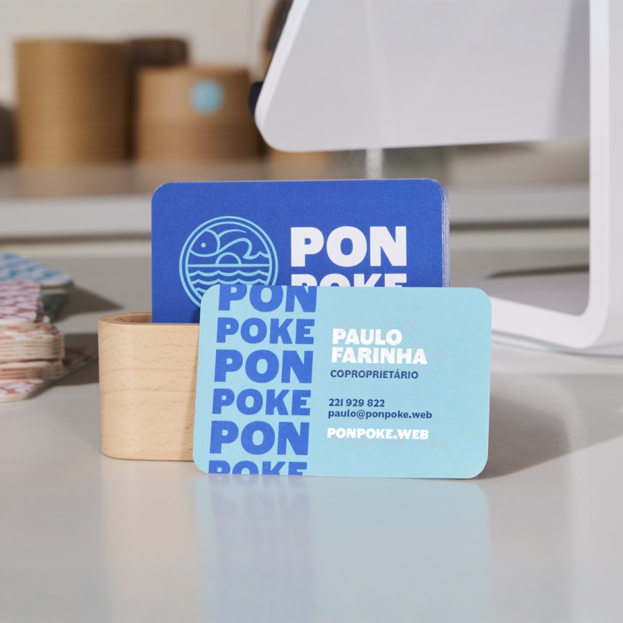 Um conjunto de cartões de visita com cantos arredondados azuis e brancos para um restaurante de poke, sobre um balcão de pagamento.