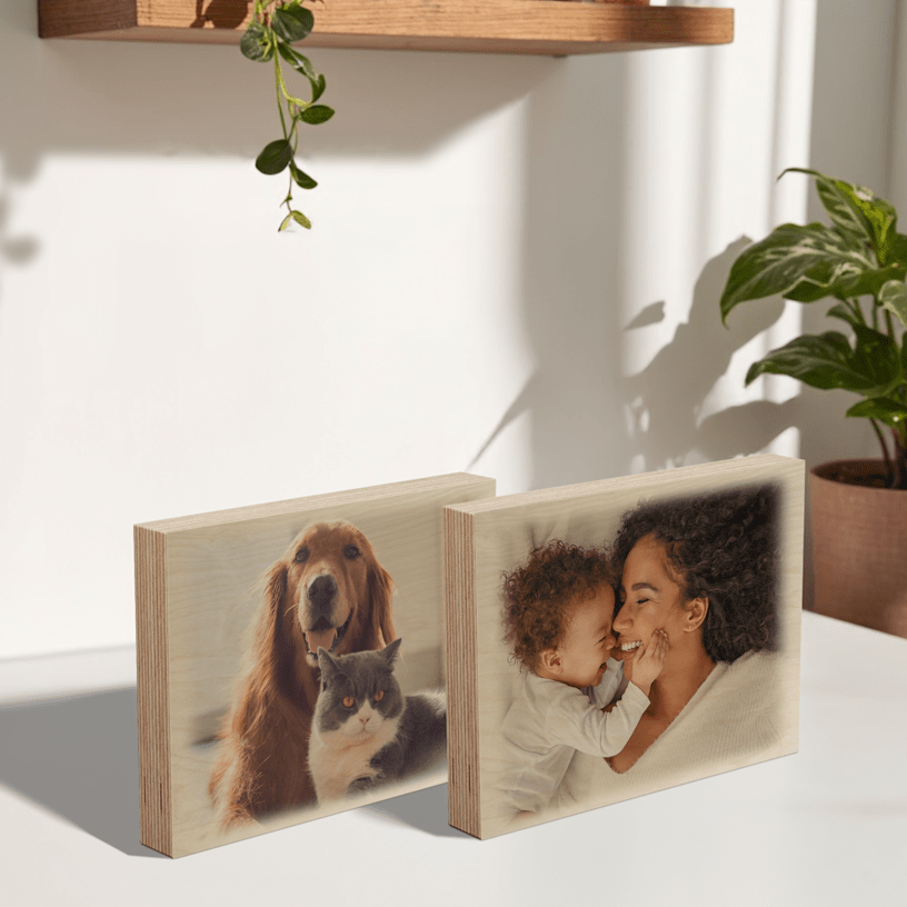 Duas impressões de fotos em blocos de madeira expostas numa mesa. Uma impressão mostra uma mãe com um bebé e a outra mostra uma foto de um cão e um gato. 