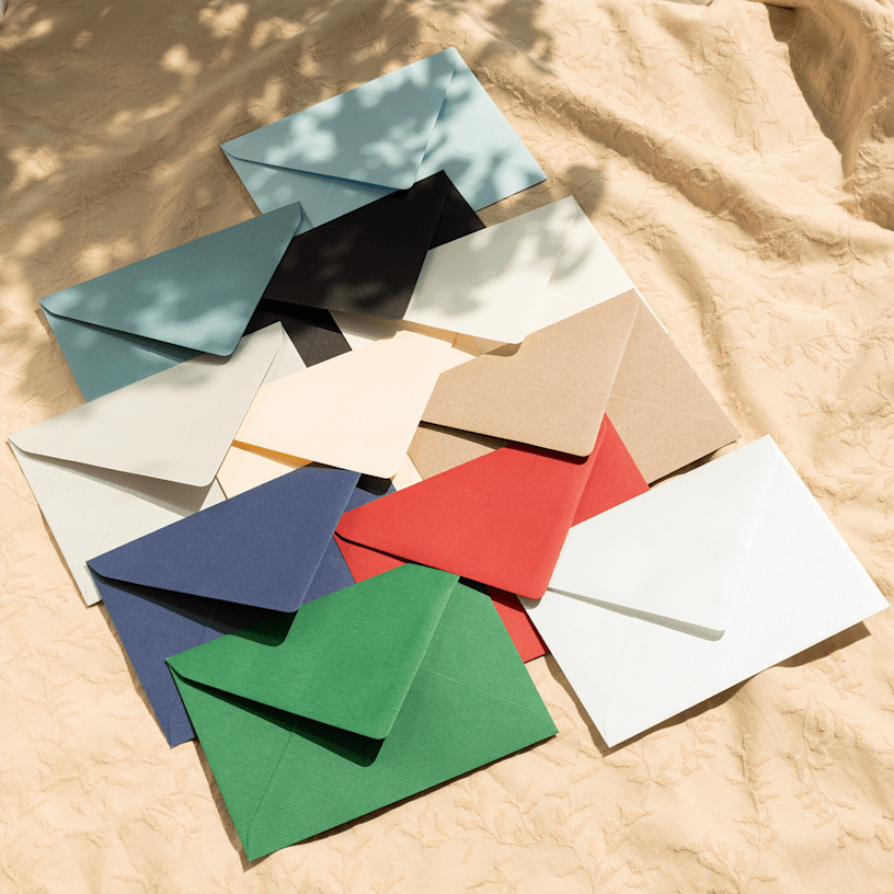 Vários envelopes coloridos dispostos sobre uma toalha de mesa texturizada de cor creme. 