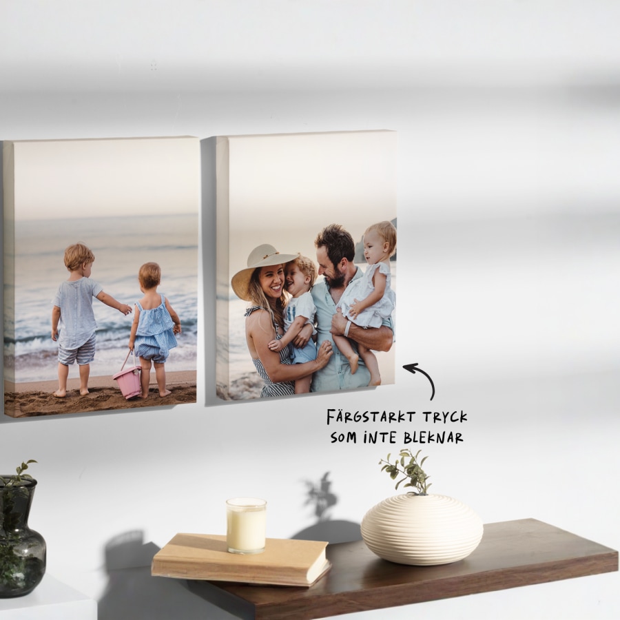 Två specialdesignade kanvastavlor upphängda på en vägg föreställande en familj på en strand samt en notering att kanvastavlorna har ett ljust och färgäkta tryck. 