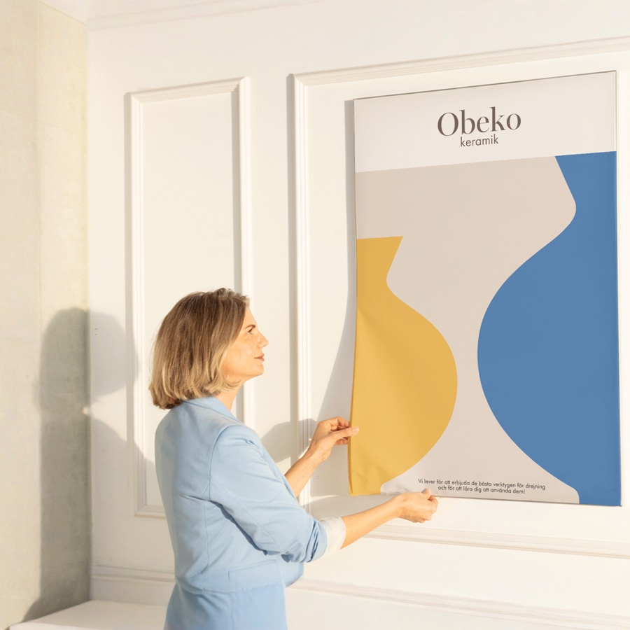 En kvinna som sätter fast ett nytt textiltryck med reklam för en krukmakare i ramen, där det fästs utan att kanten syns.