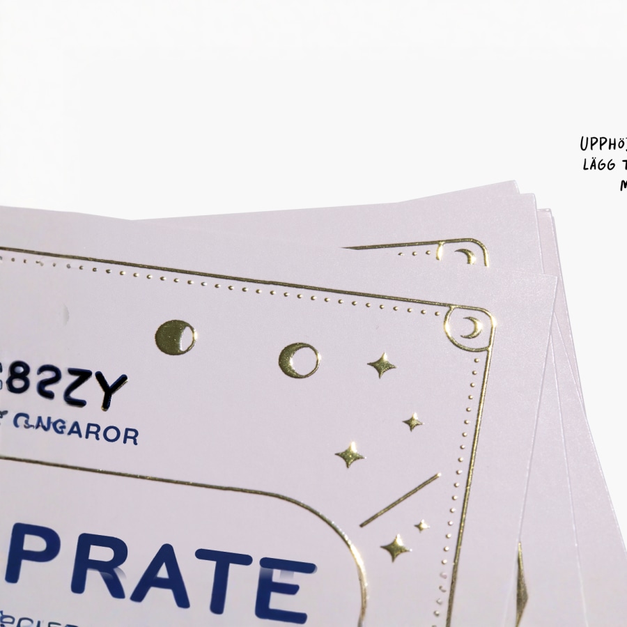 Närbild på ett visitkort med upphöjt guldfärgat folietryck av logga och text.