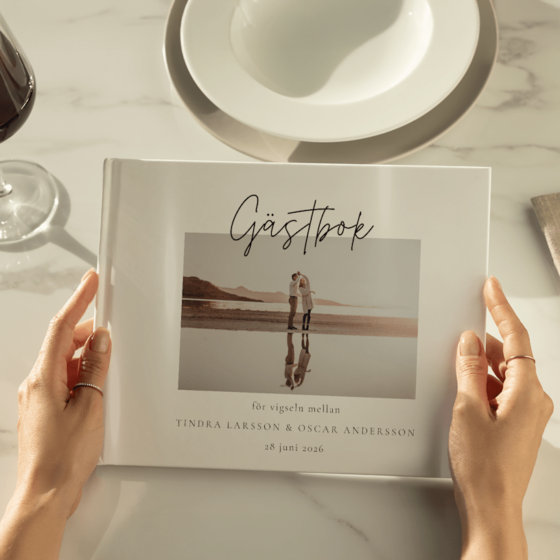 Händer som håller en bröllopsgästbok med ett foto av paret på omslaget. 